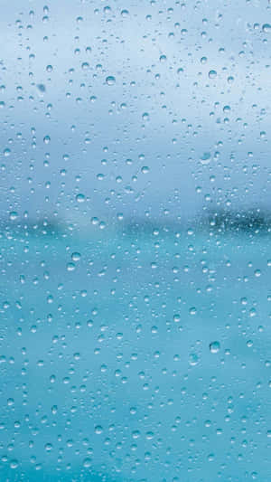 玻璃上的雨滴與模糊的藍色海洋和天空景觀
