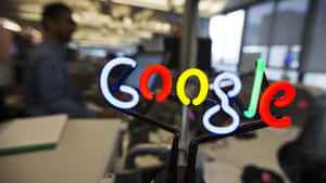 現代辦公室桌上的霓虹Google標誌，後面有模糊的員工。