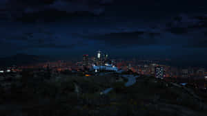 從山坡上俯瞰的夜景城市景觀，帶有發光的燈光和星空。