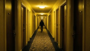 一個人在燈光昏暗、帶黃色照明的酒店走廊上行走。