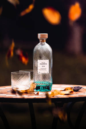 在溫暖的傍晚光線下，馬賽克桌上放著一瓶氈酒和玻璃杯，伴隨著秋葉。