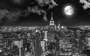 滿月下夜間城市天際線的黑白景觀。