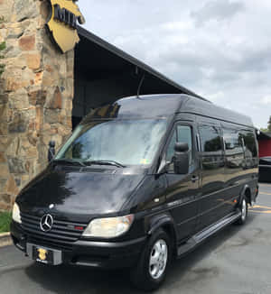 黑色 Mercedes-Benz Sprinter 客貨車停泊在石建築物入口處。 — Honor Magic V Flip 2 壁紙