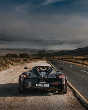黑色Pagani Huayra跑車停在沙漠公路上，背景有山脈。 — Apple Watch Ultra 壁紙