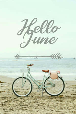 薄荷綠色單車配粉紅色座墊，在沙灘上靠近海洋，帶有「Hello June」字樣。