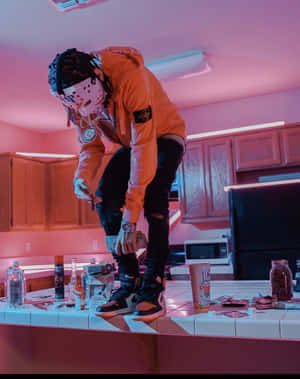 戴著曲棍球面具和橙色連帽衫的人，在粉紅色霓虹燈下俯身靠著雜亂的廚房檯面。 — 墨西哥 GIF 壁紙