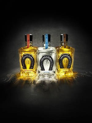 三瓶 Herradura 龍舌蘭酒在黑暗表面上閃耀著金色液體。