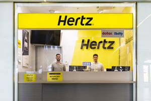 兩位Hertz員工在帶有黃色品牌的租車櫃檯。