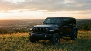 黑色Jeep Wrangler停放在長滿草的山丘上，俯瞰日落時分的山谷