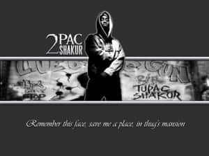 Tupac Shakur 穿著連帽衫，站在塗鴉牆前，牆上有紀念標籤。