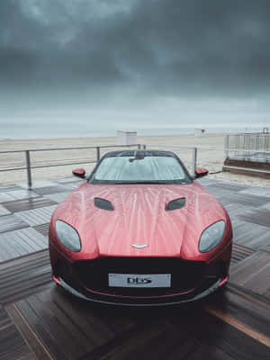 暴風雨天空下，雨中的木製碼頭上的紅色Aston Martin DBS，靠近海灘 — Kindle Paperwhite 壁紙