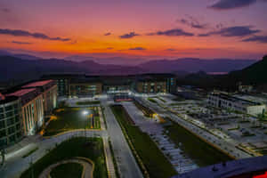 黃昏時亮燈的現代校園建築，背景有山脈。 — MacBook Pro M3 壁紙