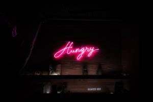 粉紅色霓虹燈牌，上面寫著「Hungry」，位於酒吧架子上方的深色木牆上。
