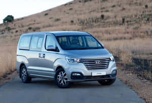銀色現代HI Bus客貨車停泊在鄉村道路上，背景有乾草山丘。