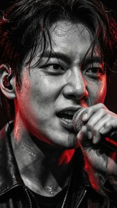 一個臉上流汗的男歌手在紅色舞台燈光下對著麥克風演唱。