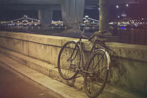 一輛單車在夜晚靠著河邊的石欄杆，背景中城市燈光閃爍。