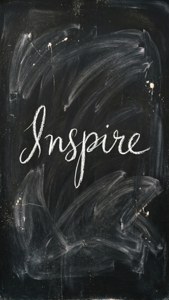 黑色黑板上以白色草書寫著「inspire」一詞，並帶有粉筆污跡。