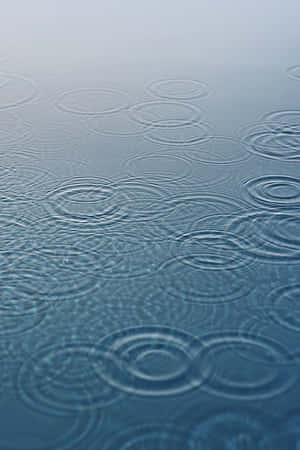 雨滴在平靜水面上形成漣漪的特寫。