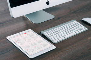 銀色 Apple iMac 鍵盤和平板電腦在深色木桌上顯示日曆