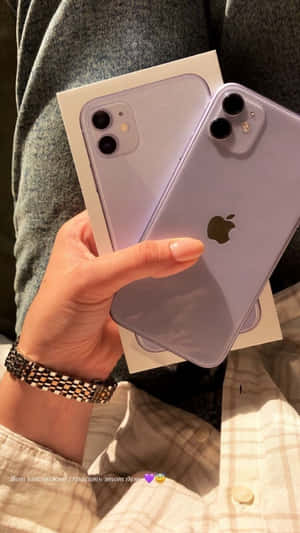 手拿薰衣草色 iPhone 11 Pro 連盒子，背景是格仔襯衫和灰色布料。