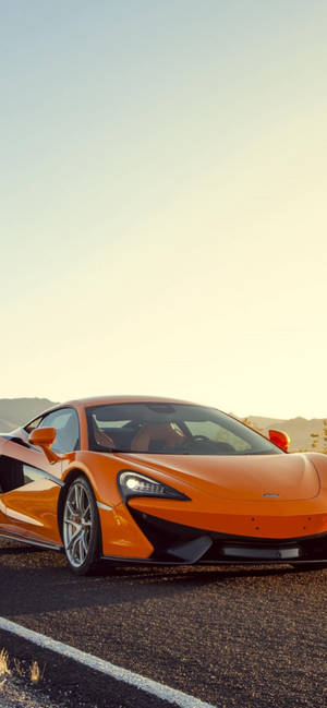 橙色McLaren跑車在金色日落時分的沙漠公路上。 — iPhone 17e 壁紙