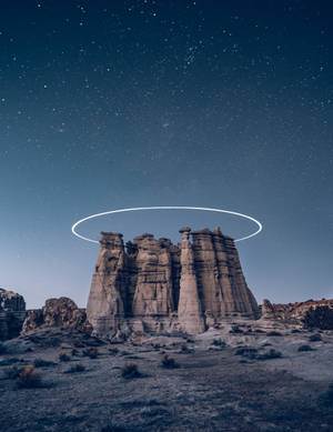 在繁星夜空下帶有發光光環的沙漠岩石形態。 — iPhone 7 Plus 壁紙