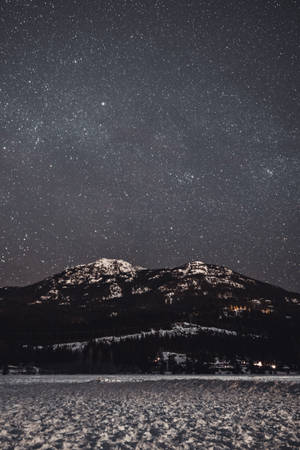 星空下被雪覆蓋的山脈，遠處村莊的燈光。 — iPhone 7 Plus 壁紙