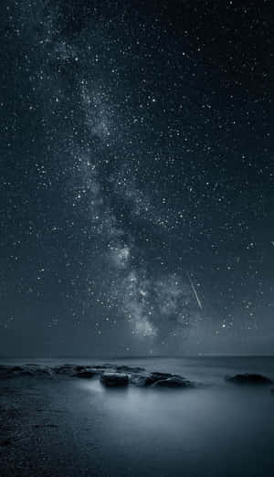 星空下，銀河系在黑暗的海洋和岩石上方