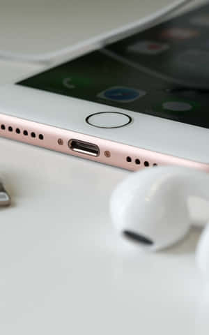 玫瑰金iPhone配白色耳機放在白色桌面上。