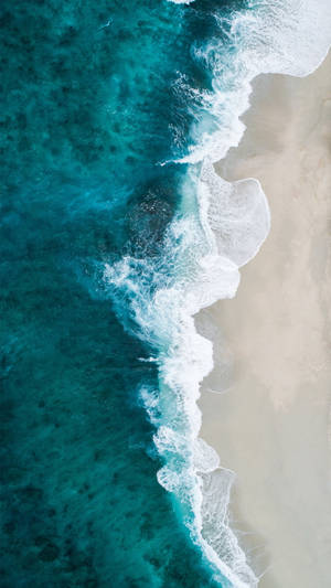 碧綠色的海浪在對角線的海岸線上與淺色沙灘相遇。