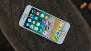 白色 iPhone 6s 在木桌上顯示主屏幕及應用程式圖示。
