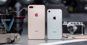 兩部金色和銀色的iPhone放在桌子上，配有復古相機和筆記本。