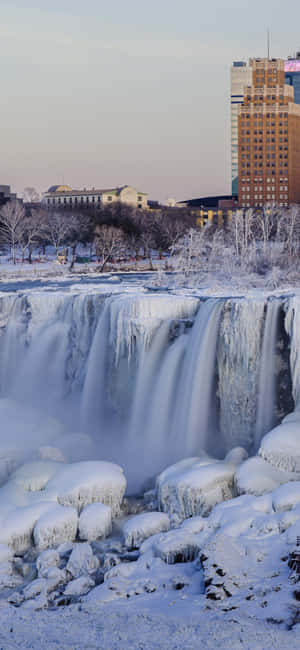 冰凍瀑布被雪和冰包圍，黎明時分城市建築環繞。 — Pixel 7 壁紙