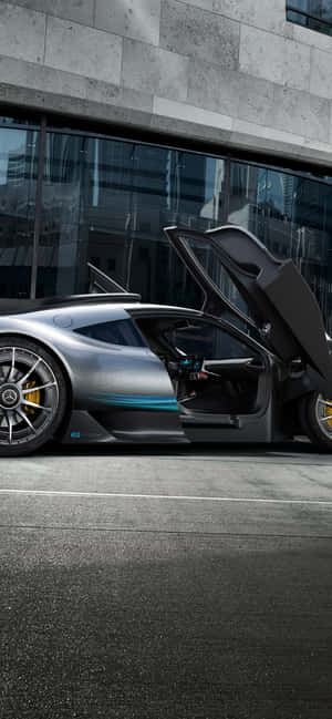 銀色跑車打開鷗翼車門，停泊在玻璃建築前。 — Infinix GT 50 Pro 壁紙