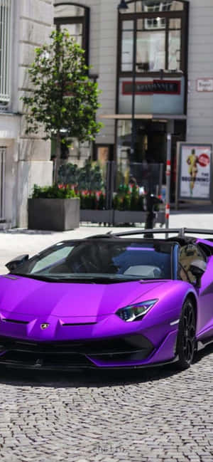 紫色林寶堅尼 Aventador 停泊在現代建築附近的鵝卵石街道上。 — Tecno Pova 壁紙