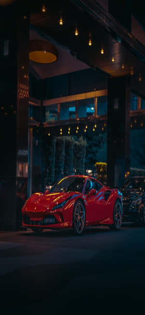 紅色跑車夜晚停放在現代建築入口處，在溫暖燈光下 — Realme Narzo Power 壁紙