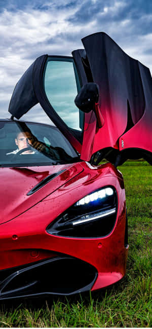 紅色McLaren跑車，鷗翼門打開，停在草地上，車內有司機。 — Galaxy M07 壁紙