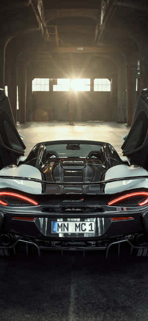 陽光普照的倉庫中，黑色McLaren跑車車門敞開。 — iPhone Air 壁紙