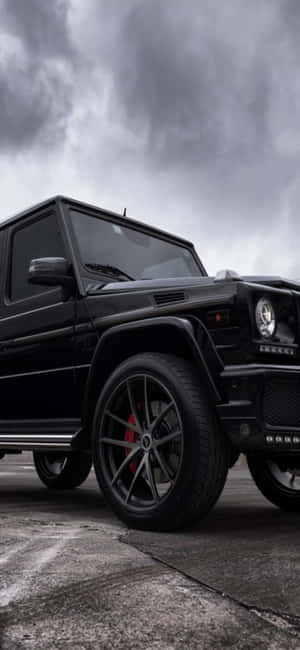 黑色Mercedes G-Wagen配備紅色制動卡鉗，停在風暴雲下的裂縫路面上。 — Pixel 7a 壁紙