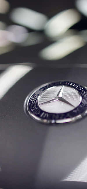 黑色汽車引擎蓋上帶有光線反射的 Mercedes-Benz 標誌特寫。
