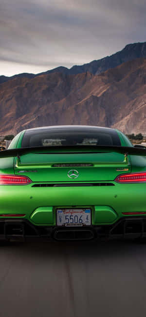 綠色 Mercedes-AMG GT R 跑車在黃昏時分行駛在山路上。 — iPhone 16 壁紙