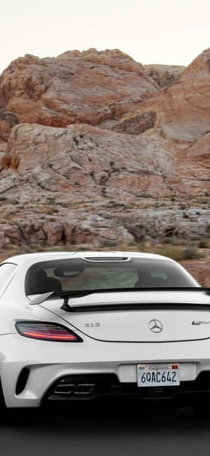 白色 Mercedes SLS AMG 在日落時分疾馳穿過紅色岩石沙漠峽谷。