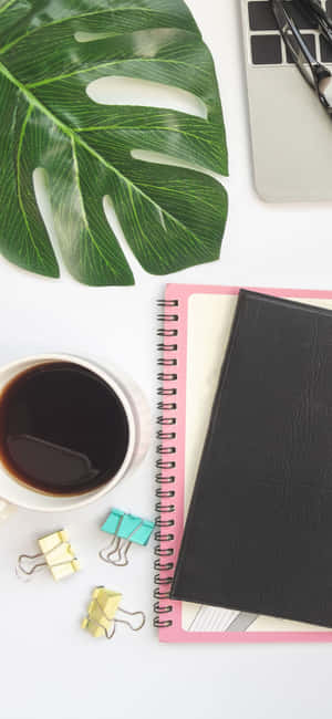 Flat lay of workspace with monstera leaf coffee cup and laptop.