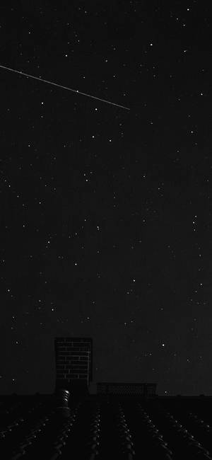 一顆流星劃過屋頂煙囪上方的繁星夜空。
