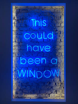 磚牆上寫著 'This could have been a WINDOW' 的藍色霓虹燈牌