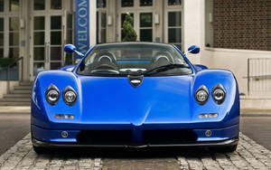 藍色Pagani Zonda跑車泊喺建築附近嘅鵝卵石街上。 — 花卉 iPhone 壁紙