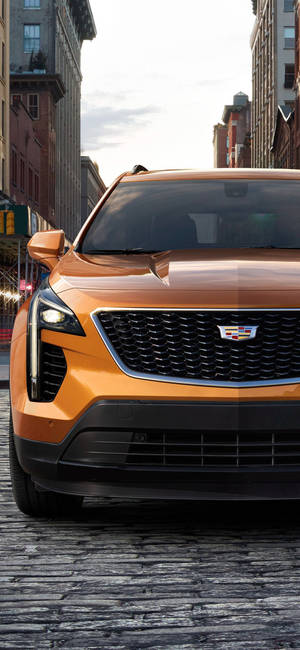 城市環境中鵝卵石街道上的橙色Cadillac SUV — iPhone 16 壁紙