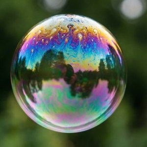 一個彩色肥皂泡在綠色背景上反射樹木和天空
