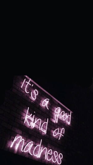 夜晚磚牆上寫住 'It's a good kind of madness' 嘅紫色霓虹燈牌。