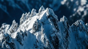 深藍色天空下，散落的雲朵襯托著尖銳的雪山山峰
